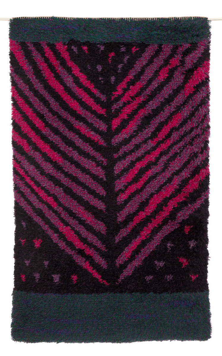 Rektangulær rye i ull med grenformet motiv bestående av striper i svart, rosa og fiolett. De horisontale partiene oppe og nede er sjattert i grønt, lilla, fiolett og blått.