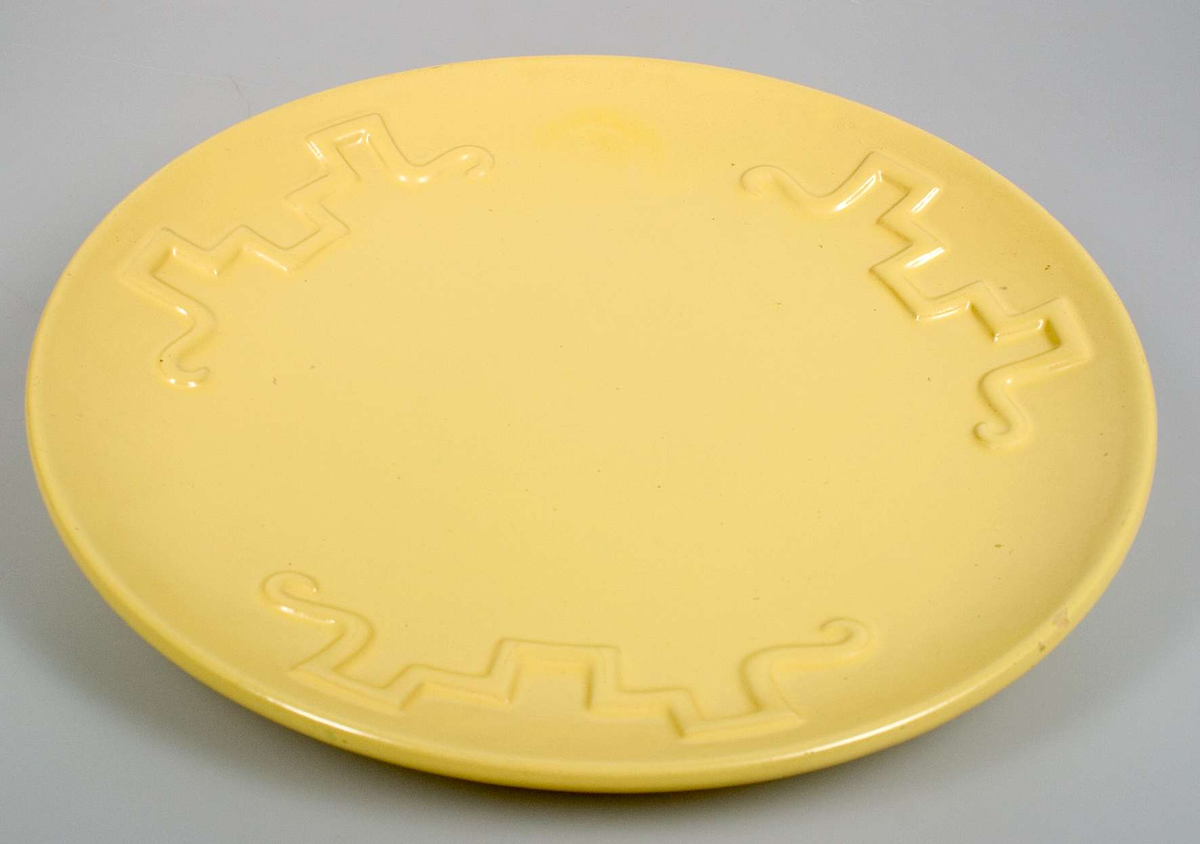 Gulglaserat runt fat med meanderslingor i relief. Stämplat: Ekeby.