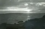 Sol bakom moln samt klippor i förgrunden vid havet i Torekov, Skåne 1922.