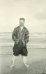 Tandläkare Gunnar Högberg stående på en strand med badrock och regnrock vid Liseleje strand, Danmark 1925.