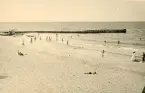 Badgäster vid strand samt en pir som går ut i havet vid Liseleje strand, Danmark 1925.
