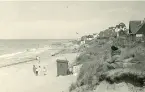 Badort med sandstrand med de ikoniska badhyttorna samt hus som på höjden med sin närhet till havet vid Tisvilde, Danmark 1925.