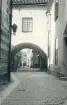 Bilden visar en smal gränd med kullerstensbeläggning och en karaktäristisk överbyggnad/valv i Visby, Gotland 1927.