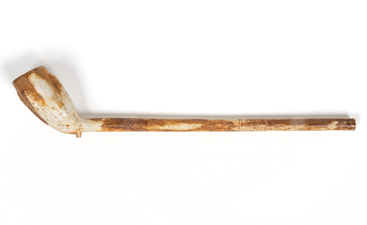 Rak med orneringar runt huvudets kant och skaft, längsgående vulster på huvudet. Avbruten, 295 mm från änden, i två delar, båda delarna bibehållna.