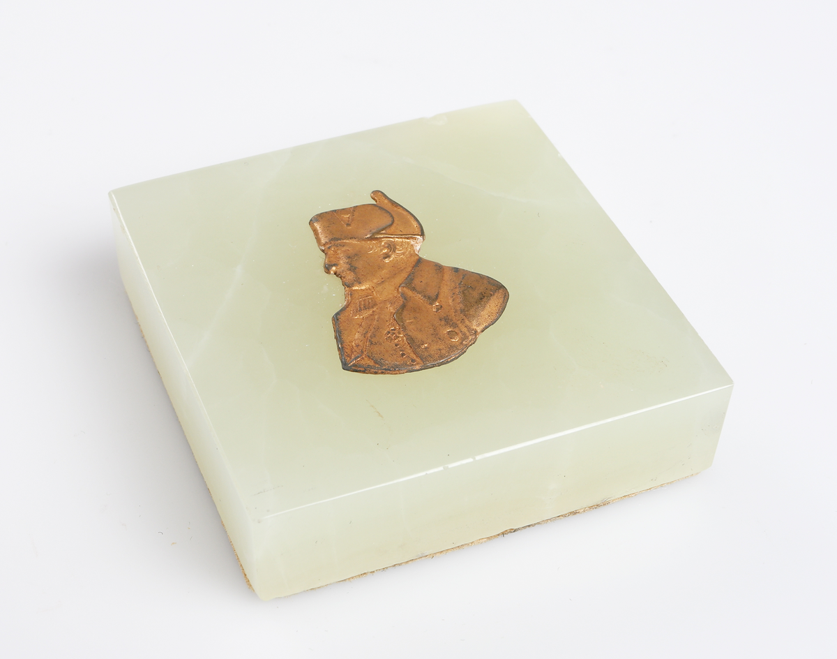 Kvadratisk brevpress av grön marmor med Napoleon i relief i gul metall. 

Insrivet i huvudbok år 1969.