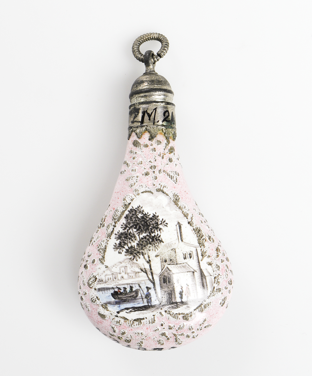 Luktflaska av rosafärgat porslin. Bild av träd och byggnad vid vatten med personer i båt, snarlika motiv på båda sidor. Droppformig med skruvkork av vit metall. För förvaring av luktsalt. 

Inskrivet i huvudbok år 1969.