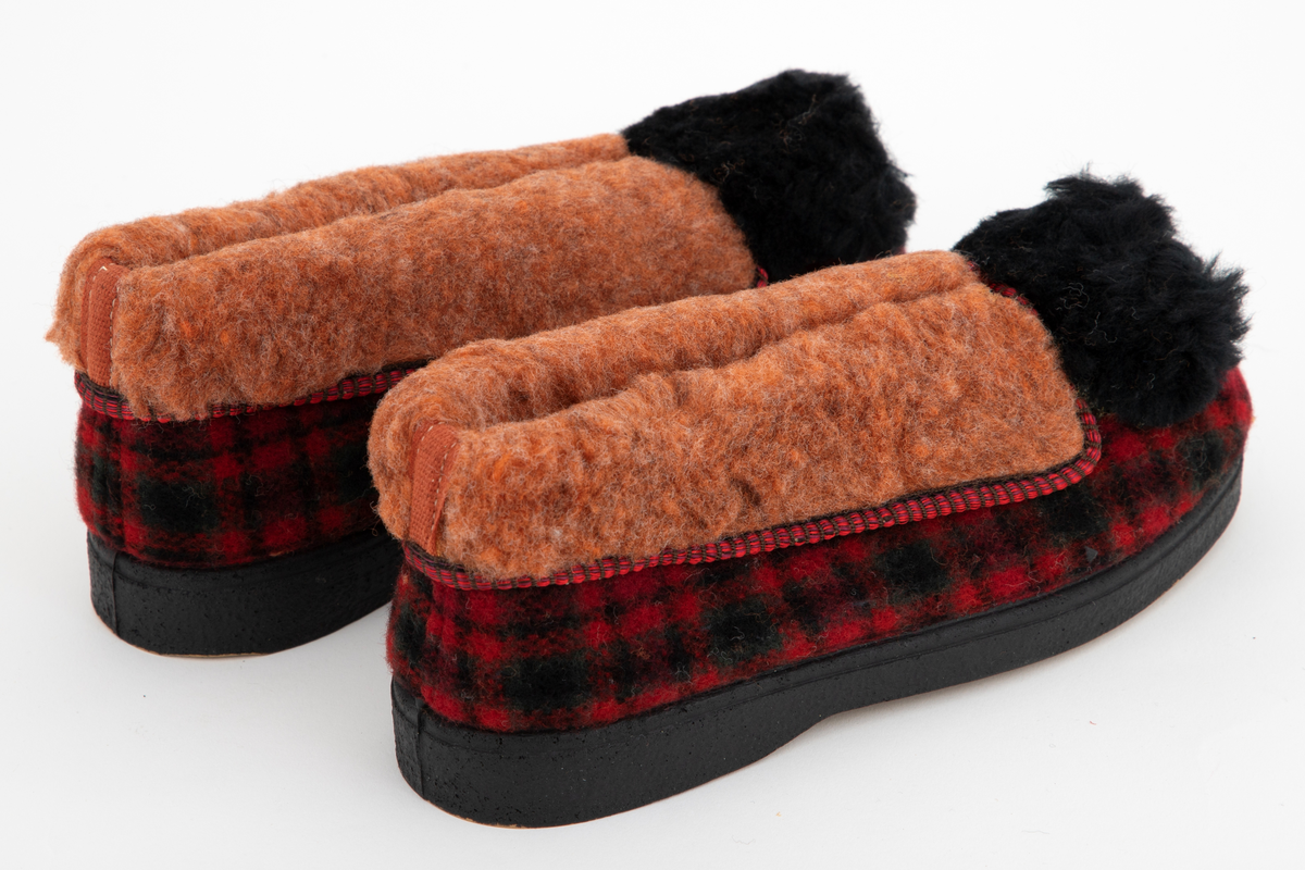 Tøfler i rutete ull i rødt, svart og grønt med nedbrettet og limt overkant i rødbrun, lodden viskosepels. Tøflene er innvendig fôret med samme materiale. Stor svart pompong på forstykket.
