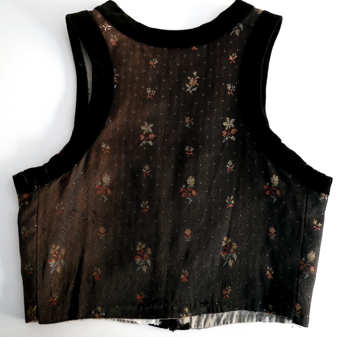 Livet er svart i botn med spetter og grøne og rosa blomar. Livet har v-forma opning framme og kring armhol og opning er det svarte fløyelsband. Liver er fora med beige bomullsstoff. 