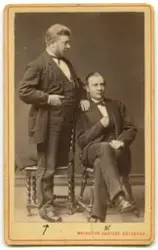 Porträtt på två män i helfigur, en sittande och en stående.