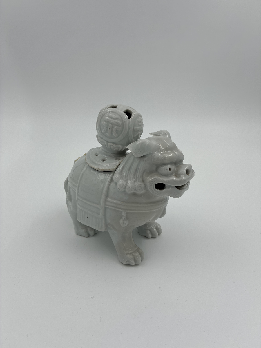 Prydnadsfigur i form av hund i kinesisk stil.
Figuren är ihålig och har på ryggen en öppning försedd med ett lock. 
Locket har en stor, delvis genombruten knopp prydd med fyra kinesiska skrivtecken i relief.
Vit glasyr.

Funktion: Möjligen rökelsekar