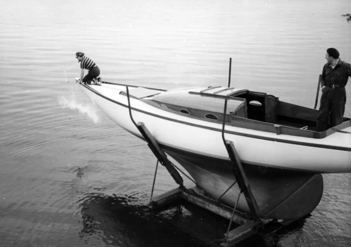 Sjösättningen av Fritiof Colbings egenbyggda segelbåt "Sigrun". Båten står på en ställning i vattnet, i fören sitter Kerstin Colbing. Båten blir döpt till "Sigrun". Vid den så kallade Saltladan, som låg vid de gamla lokstallarna i Nynäshamns hamns norra område. Båten byggdes åren 1948-1951.