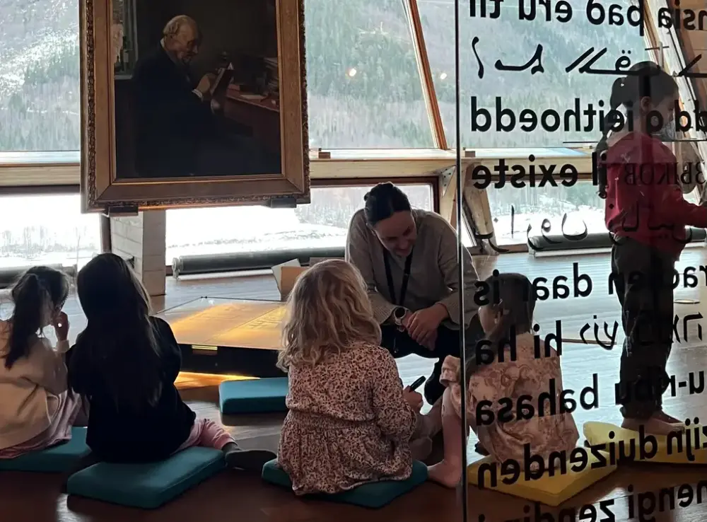Formidalar frå Aasentunet har samla ei gruppe med barn frå ein av barnehagane i Ørsta framfor måleriet av Ivar Aasen i utstillinga i Aasentunet. Formidlaren fortel om Ivar Aasen.