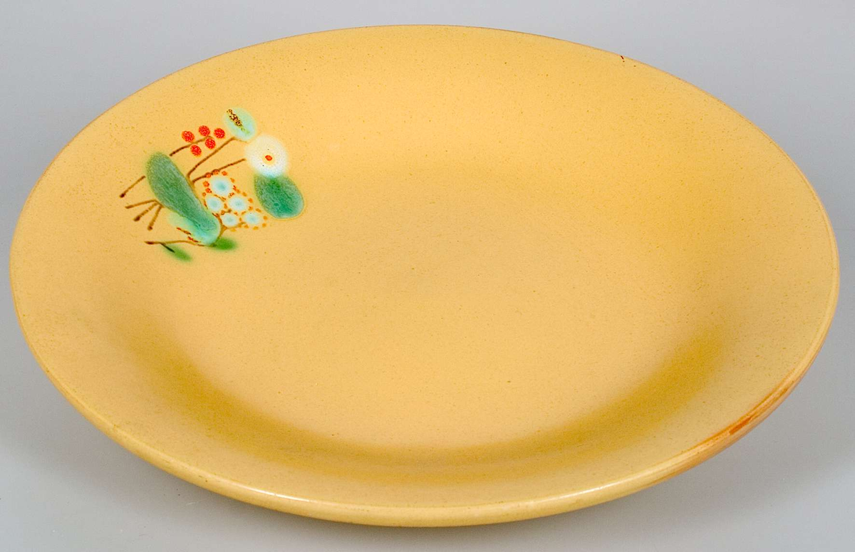 Fat, glaserat med matt gul glasyr och dekorerat på kanten med ett litet abstrakt motiv i grönt, rött, ljusblått och vitt. Stämplat otydligt EKEBY.