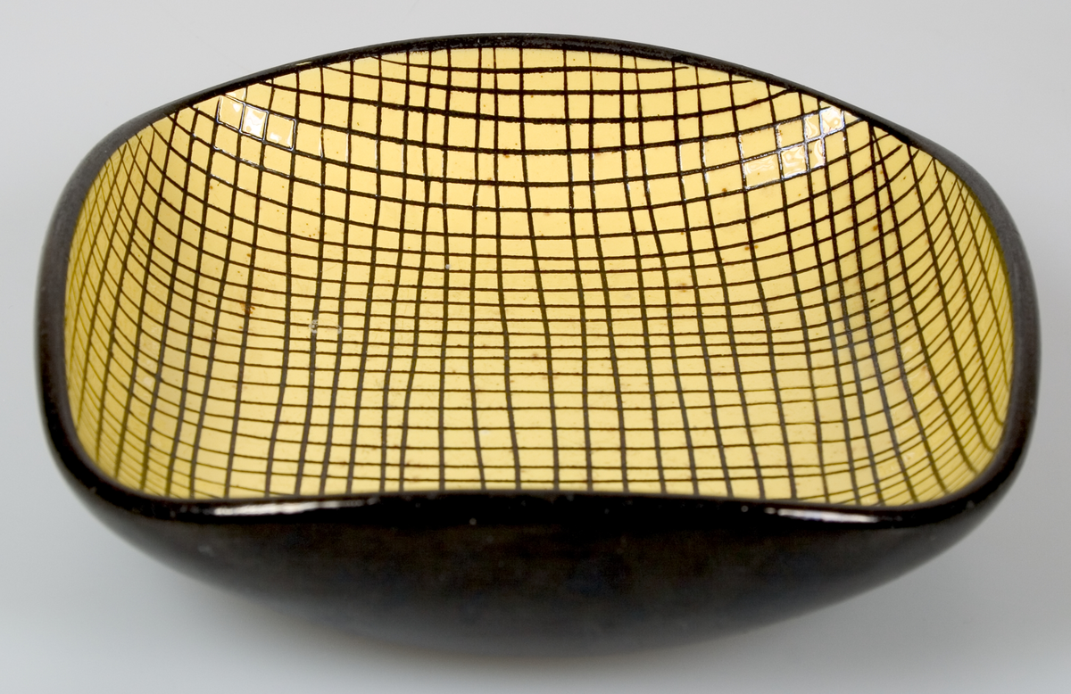 Litet fat med uppåtvikta kanter så att fatet blir fyrkantigt. Svart glasyr på utsidan och gul på insidan. I den gula glasyren ristat svart rutmönster.
Rund stämpel i botten: UE, 2195, Abg.