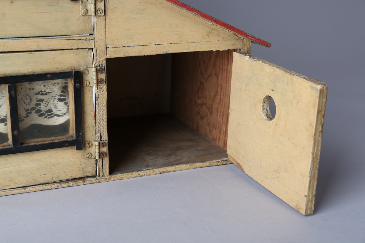 Rektangulært dukkehus i treverk med tre vegger, festet tak og dører i front. Huset er gult på utsiden og har tre etasjer, hvor loftet er lukket, men har et mindre hull i front. Taket er rødt. Dørene har vinduer med brunt listverk og hvite blondegardiner på innsiden. Tre gulvflater er belagt med grå linoleum, to gulvflater mangler belegg. Fire av rommene har tapet på veggene, alle i rikt detaljerte mønstre i flere farger. Taket i andre etasje har et hvitt intrikat mønster. Tomme rom uten særlige tegn til bruksområder.