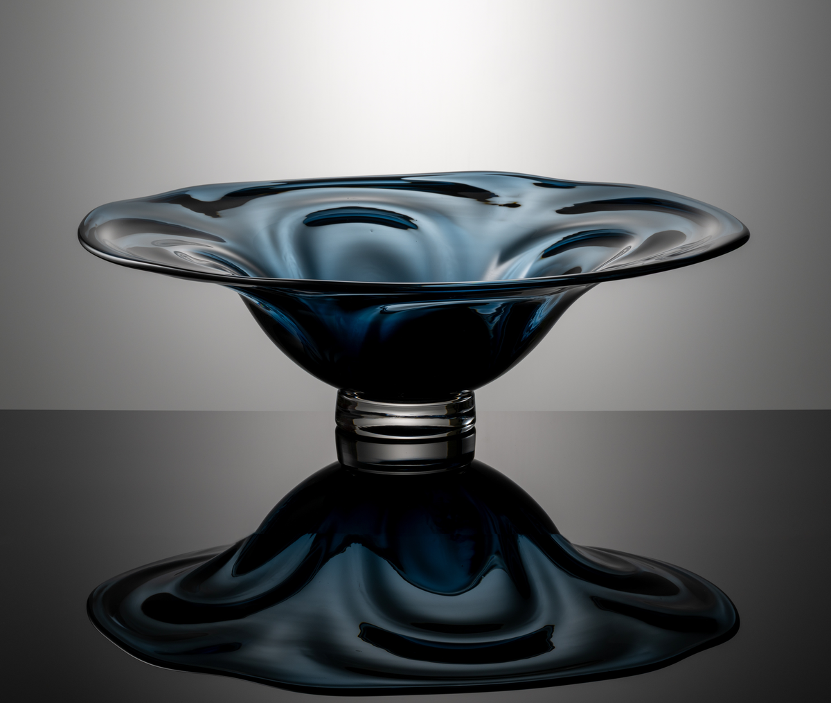 "Vattenspel" Formgivare: Lars Hellsten. Skål med optik. Klockformad med generöst utvikt brätte och något oregelbunden mynningskant. Blågrått klarglas med ofärgad låg fotklack.