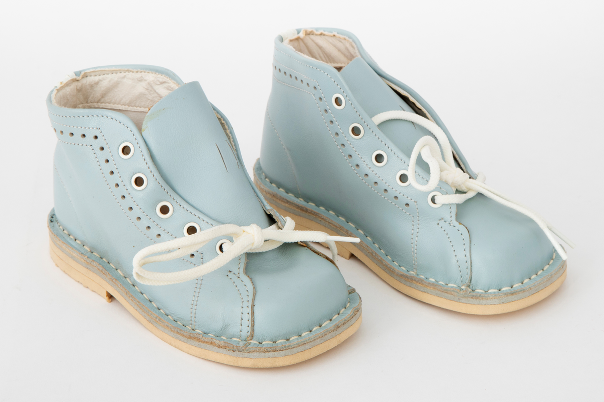 Snøresko til barn i lyseblått skinn med hvite sømmer og hullmønster i sidene. Snøring i 5 x 2 hull med hvite maljer og runde, hvite lisser. Hvit fôr og hvite såler. Originaleske med Disneymotiv følger med.