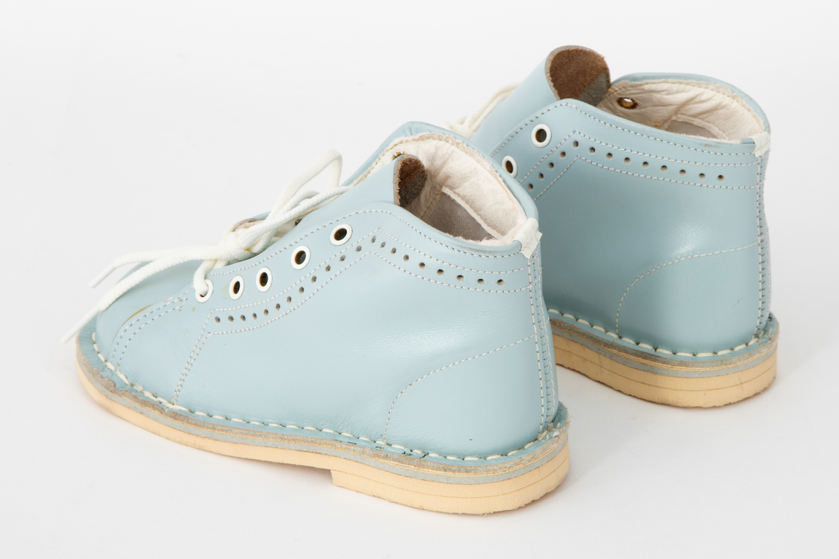 Snøresko til barn i lyseblått skinn med hvite sømmer og hullmønster i sidene. Snøring i 5 x 2 hull med hvite maljer og runde, hvite lisser. Hvit fôr og hvite såler. Originaleske med Disneymotiv følger med.