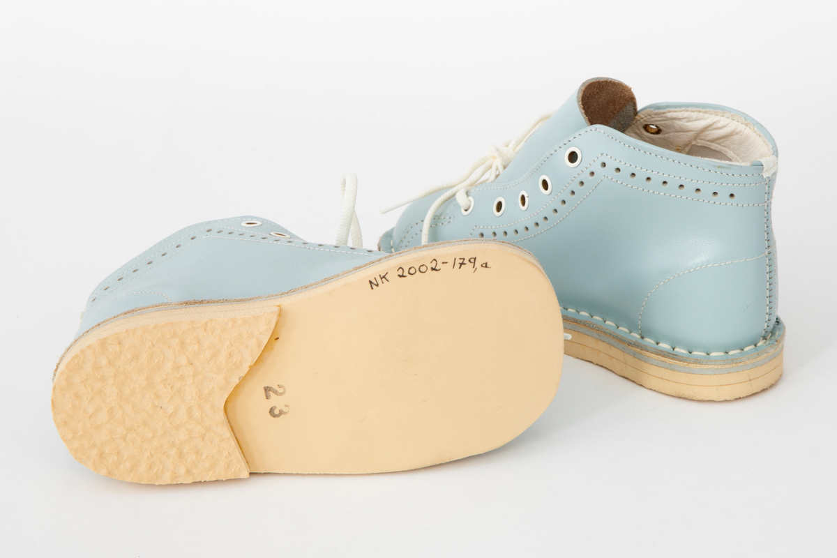 Snøresko til barn i lyseblått skinn med hvite sømmer og hullmønster i sidene. Snøring i 5 x 2 hull med hvite maljer og runde, hvite lisser. Hvit fôr og hvite såler. Originaleske med Disneymotiv følger med.