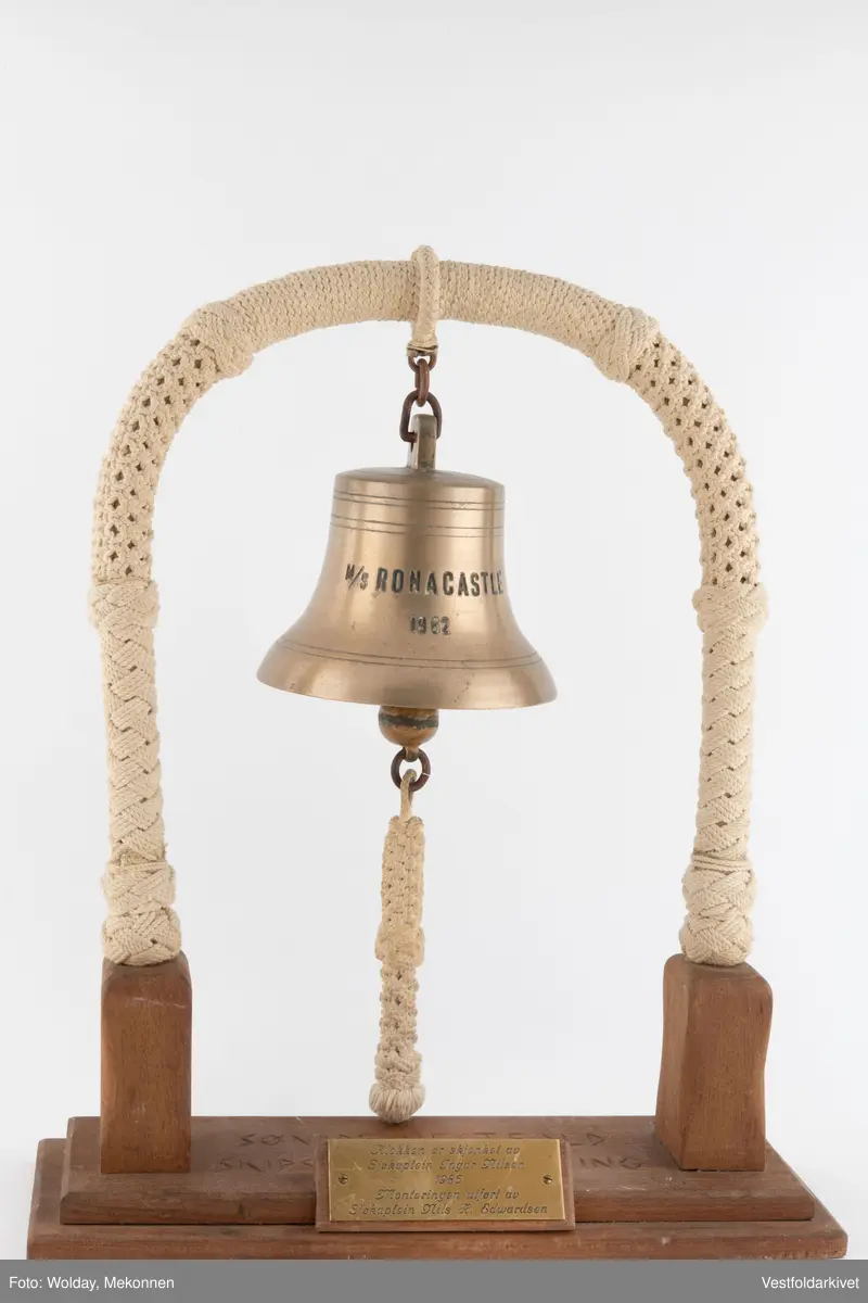 En klokke av metall, festet på et stativ dekorert med tauverk.