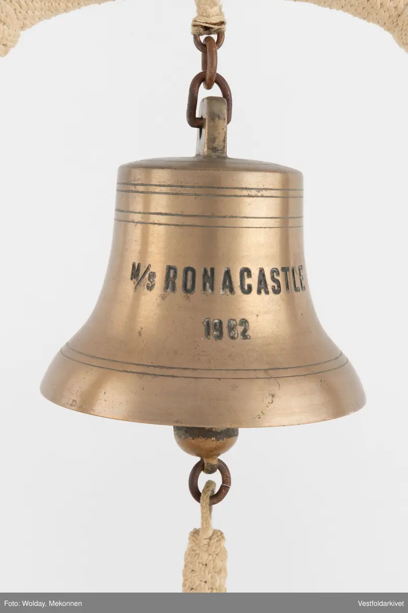 En klokke av metall, festet på et stativ dekorert med tauverk.