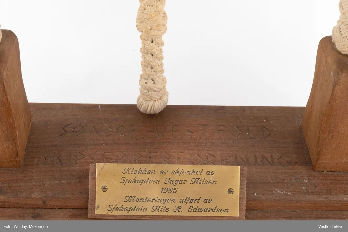 En klokke av metall, festet på et stativ dekorert med tauverk.