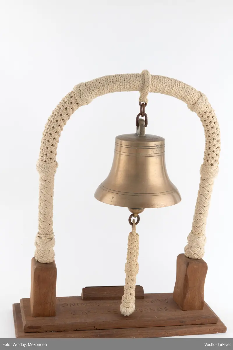 En klokke av metall, festet på et stativ dekorert med tauverk.