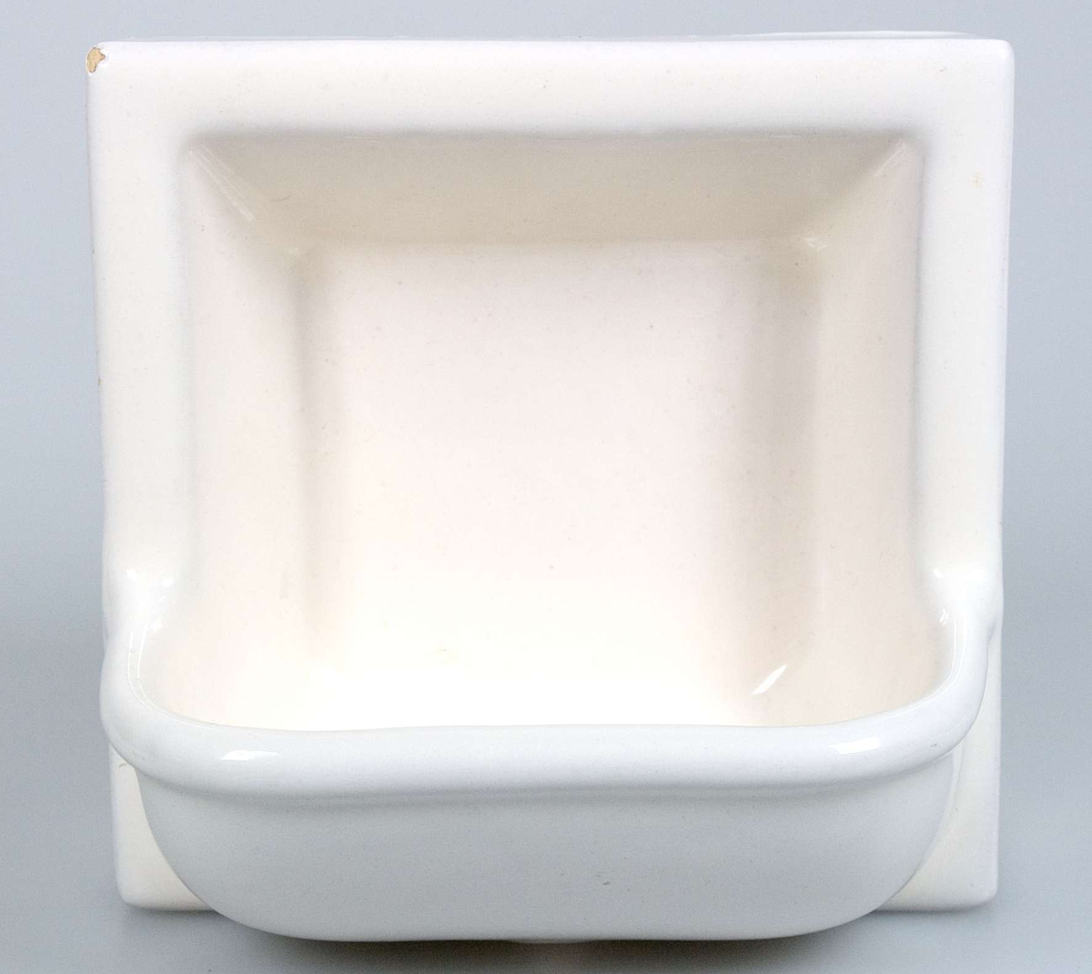 Tjock kakelplatta med tvålkopp, av gulbrännande lera med vit tenn- och blyglasyr. På baksidan 4 fötter, en i varje hörn, stämplad K 1S.