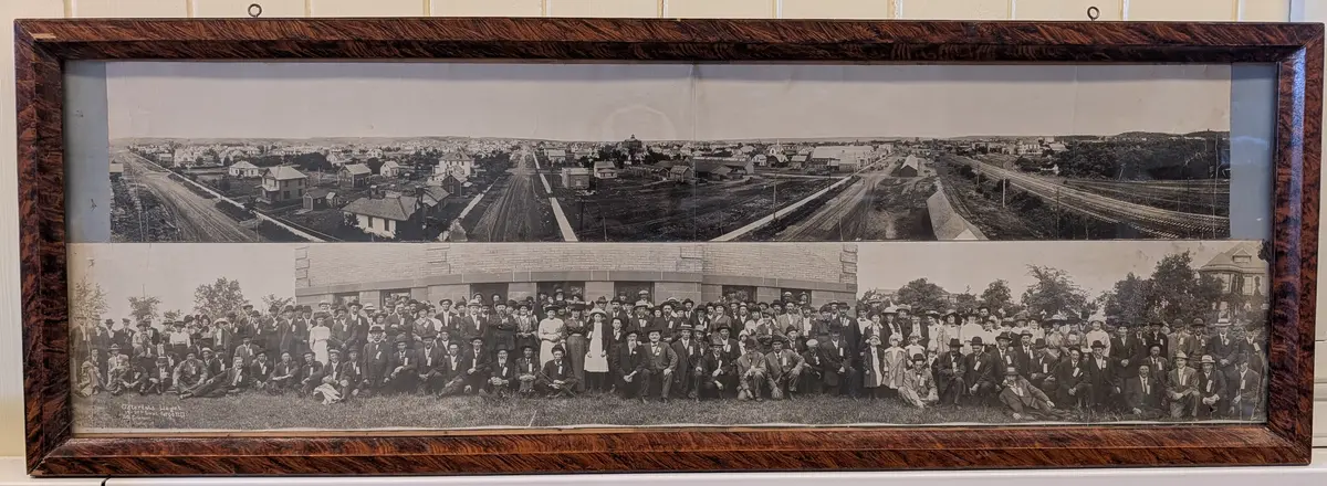 To brede fotografier innrammet. 
Foto av amerikansk by, trolig Fargo, North Dakota ("Rogers-Jeffrey Lumber co" synlig på fabrikktak).
Østerdalslaget i Fargo, North Dakota, ukjent år. Mange personer er nummerert med håndskrift. 
Fotograf er "S.O. Erickson"
