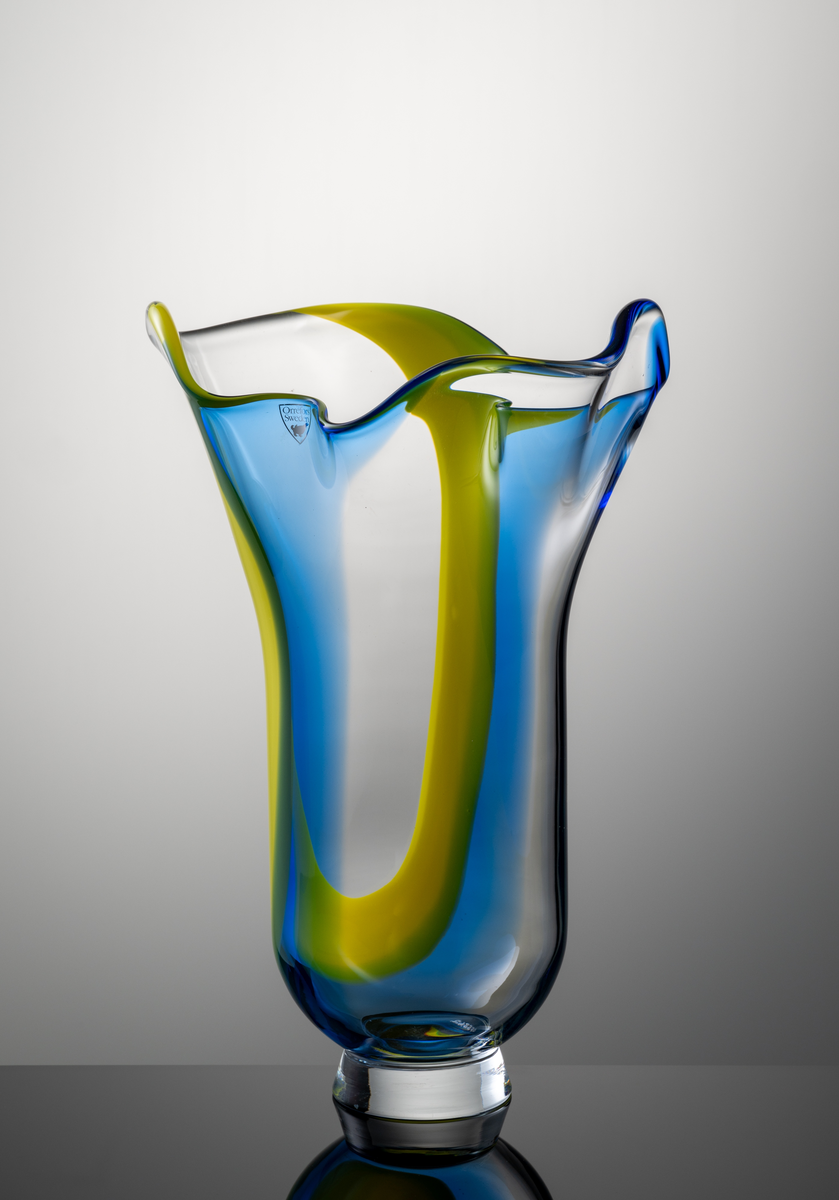 Vas med veckad, profilerad mynning. Låg fotklack i ofärgat glas. Dekor i form av ett brett färgfält i gult och blått.
Formgivare: Lars Hellsten.