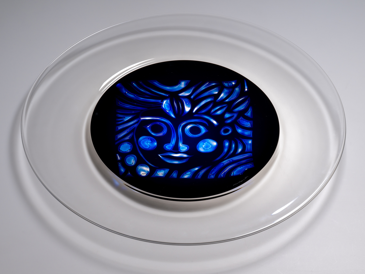 Arielfat. Stort, med rund form och klar bred bård. I mitten en blå rundel med ett stiliserat luftmönster föreställande
ett ansikte. 
Formgivare: Lars Hellsten.