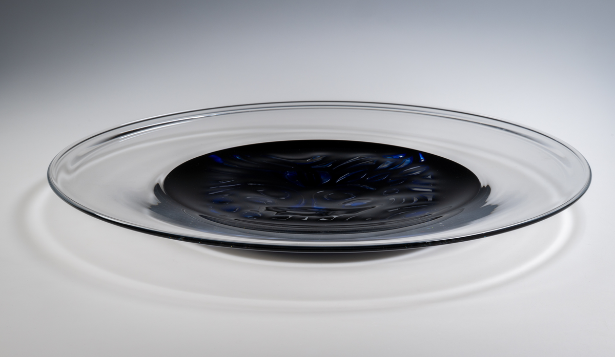 Arielfat. Stort, med rund form och klar bred bård. I mitten en blå rundel med ett stiliserat luftmönster föreställande
ett ansikte. 
Formgivare: Lars Hellsten.