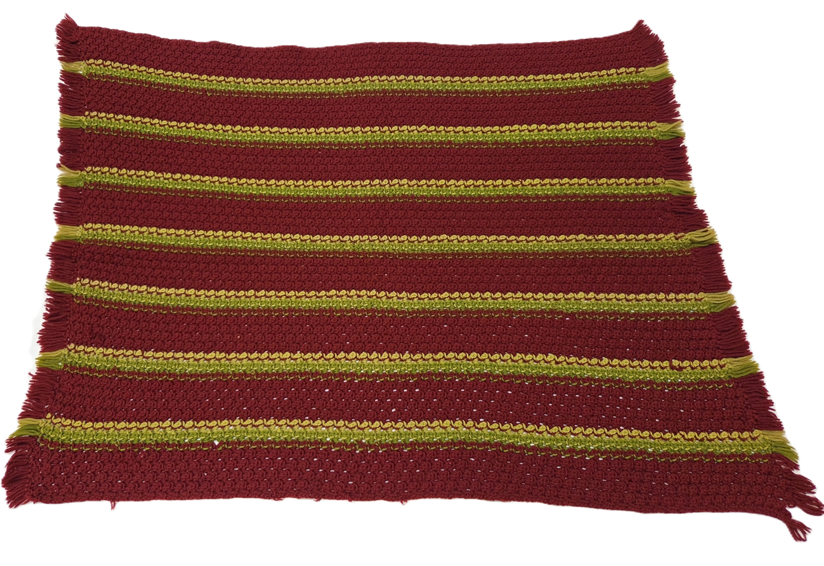 Virkad filt. Ullgarn i rött och grönt. Filten är något assymetrisk. Fransar i sidorna.