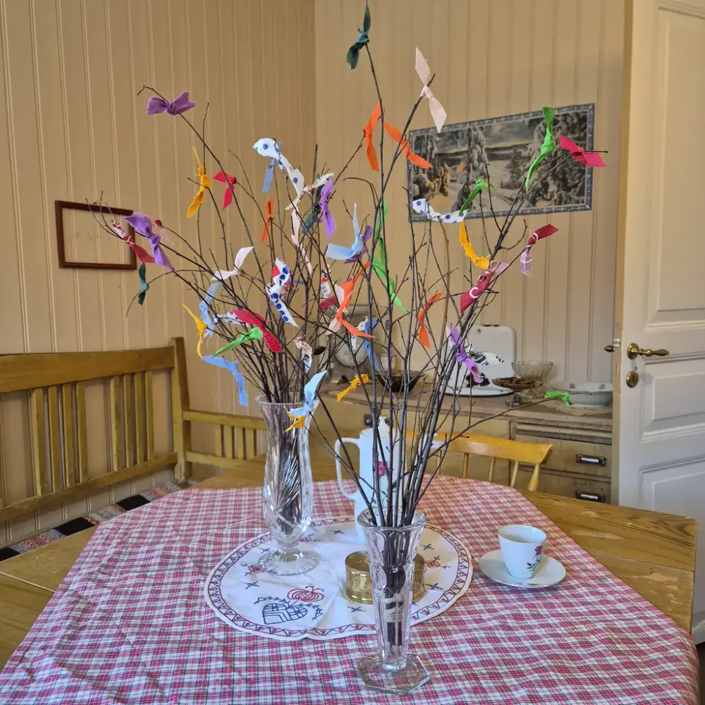 Två vaser med påskris står på ett bord med en rutig duk.