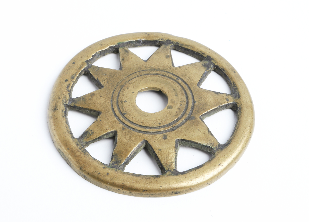 Hjulformat ornament av mässing.Förmodligen till ett betsel eller knivatyg. 

Inskrivet i huvudbok år 1873.