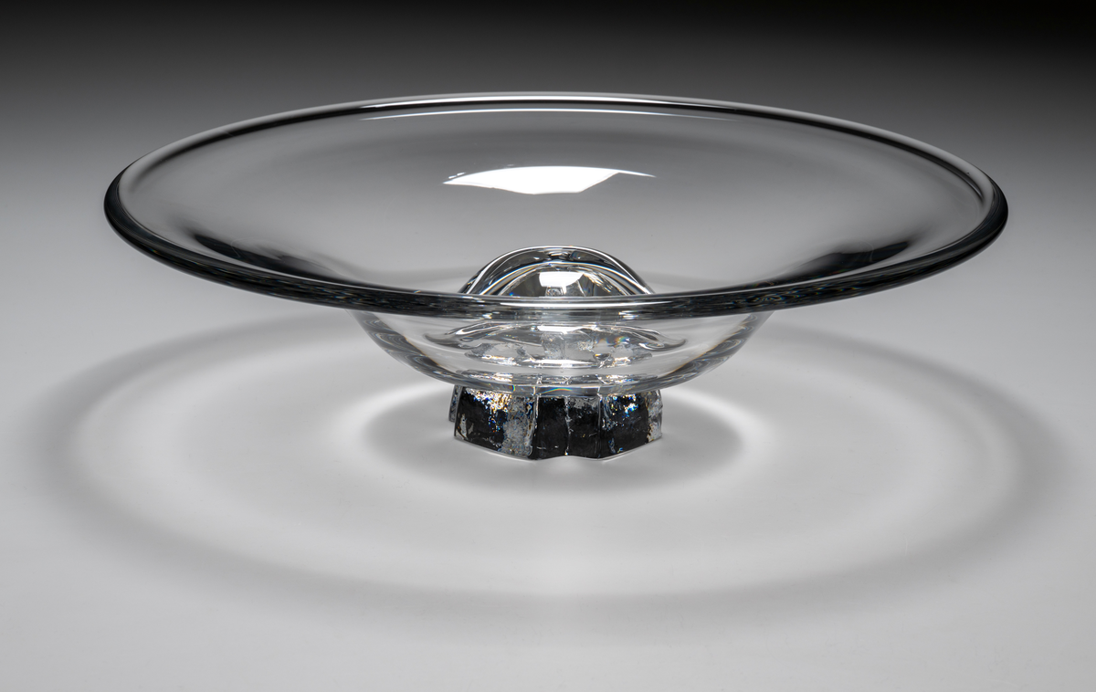 "Havsblomma" Formgivare: Lars Hellsten. Fat på fot. Klockformad övre del i ofärgat glas. Fot i form av en ”blomma” med breda räfflor. Fatet är nedtryckt över foten. Sammanfogade varmt i hyttan.