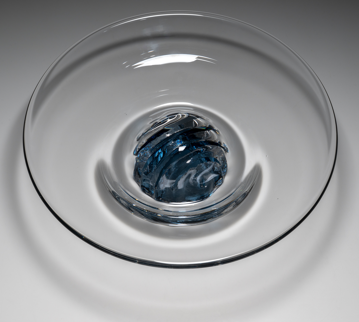 "Havsblomma" Formgivare: Lars Hellsten. Skål på fot. Klockformad övre del i ofärgat glas. Fot i form av en blå ”blomma” med breda räfflor. Fatet är nedtryckt över foten. Sammanfogade varmt i hyttan.