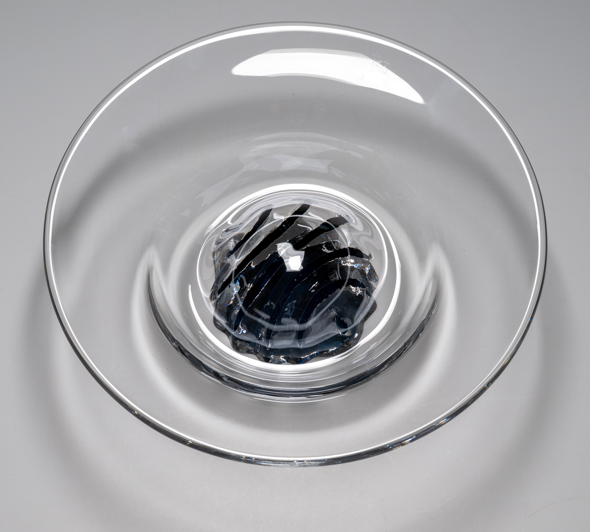 "Havsblomma" Formgivare: Lars Hellsten. Skål på fot. Klockformad övre del i ofärgat glas. Fot i form av en blå ”blomma” med breda räfflor. Fatet är nedtryckt över foten. Sammanfogade varmt i hyttan.