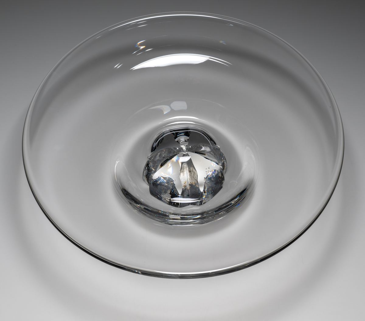 "Havsblomma" Formgivare: Lars Hellsten. Fat på fot. Klockformad övre del i ofärgat glas. Fot i form av en ”blomma” med breda räfflor. Fatet är nedtryckt över foten. Sammanfogade varmt i hyttan.