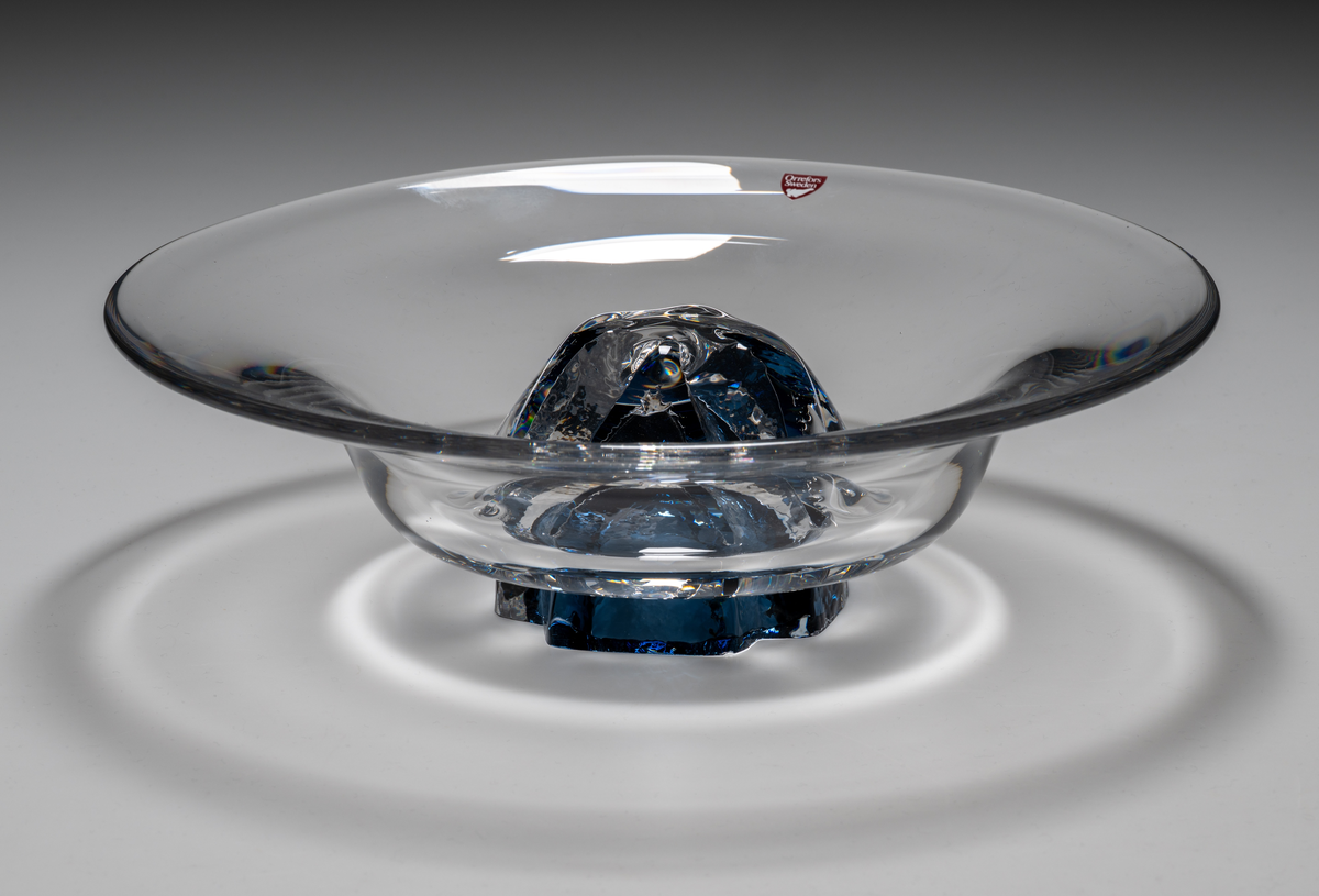 "Havsblomma" Formgivare: Lars Hellsten. Skål på fot. Klockformad övre del i ofärgat glas. Fot i form av en blå ”blomma” med breda räfflor. Fatet är nedtryckt över foten. Sammanfogade varmt i hyttan.