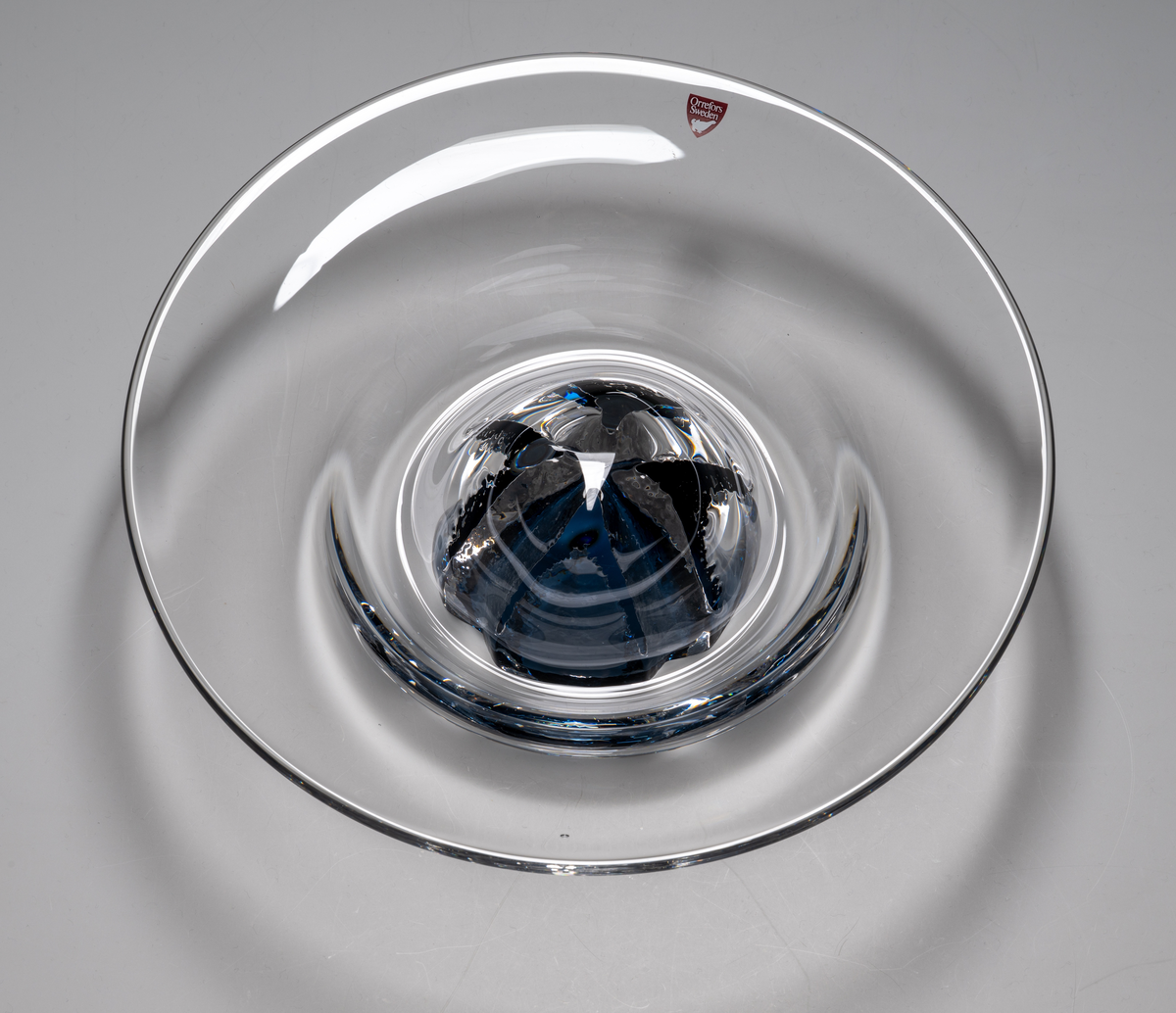 "Havsblomma" Formgivare: Lars Hellsten. Skål på fot. Klockformad övre del i ofärgat glas. Fot i form av en blå ”blomma” med breda räfflor. Fatet är nedtryckt över foten. Sammanfogade varmt i hyttan.