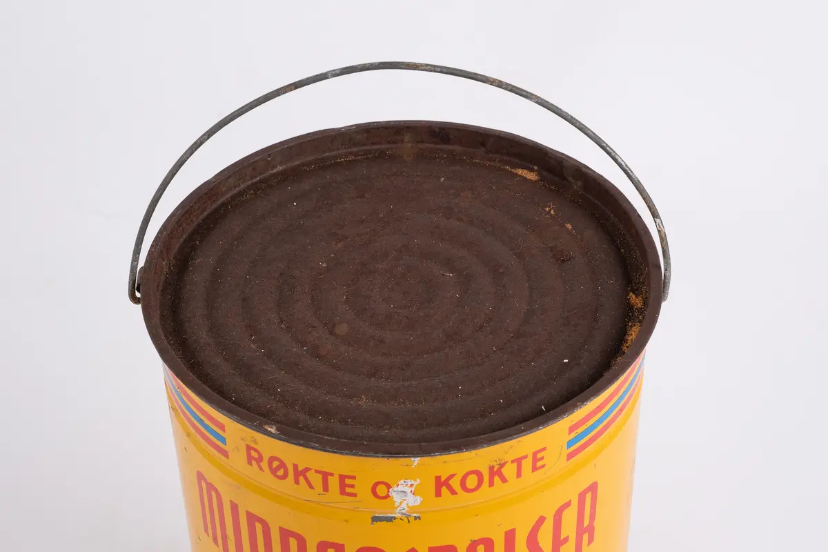 Spann. Sylinderformet. Emaljert blikkmetall. Lokk med riller. Fleksibel bøylehank i metall. Illustrasjon på 2 sider av serveringsfat med pølser. Skrift.