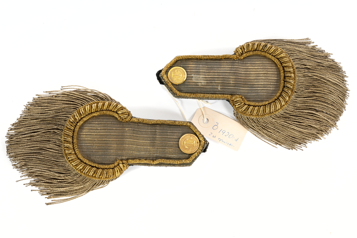 Epåletter, ett par, av guldgalon med smal träns av guld samt buljoner av smal  silvertråd. Förgylld knapp, flat, med ankare och tre kronor, fodrade med svart kläde.
Tillhör sjöofficersuniform 1808.