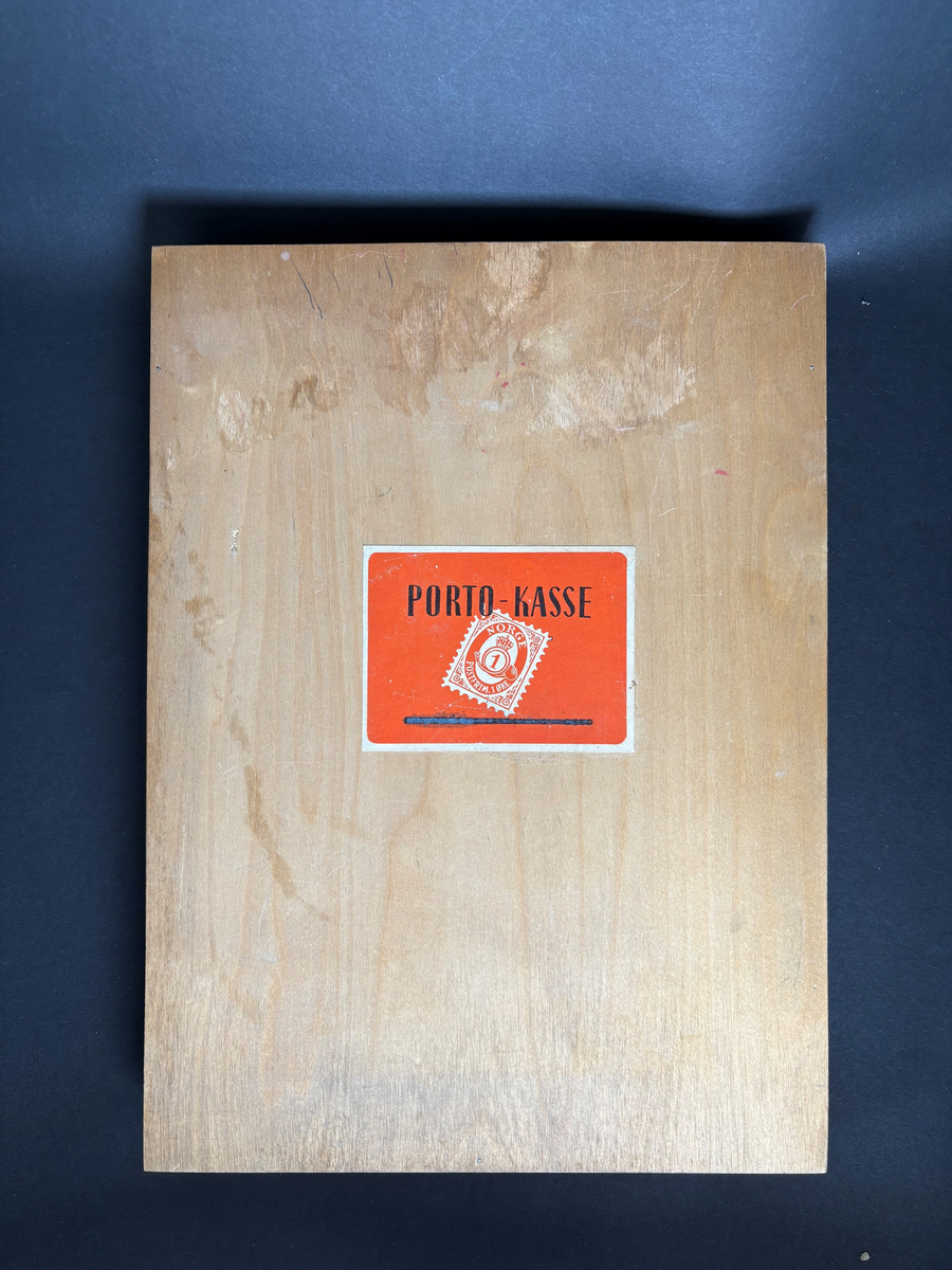 Rektangulær kasse i tre som kan åpnes med festet, stående lokk. På utsiden er det festet en rød merkelapp med motiv av et frimerke og tekst "PORTO-KASSE".

Kassen er inndelt i flere rom for oppbevaring. På innsiden av lokket er det pålimt en portotakst.