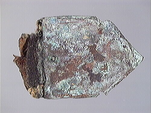 Remändebeslag av koppar med kvarsittande fragmentariska rester av läder. Lädret har fästs med stift genom beslaget. Beslaget är ärgat men relativt välbevarat.