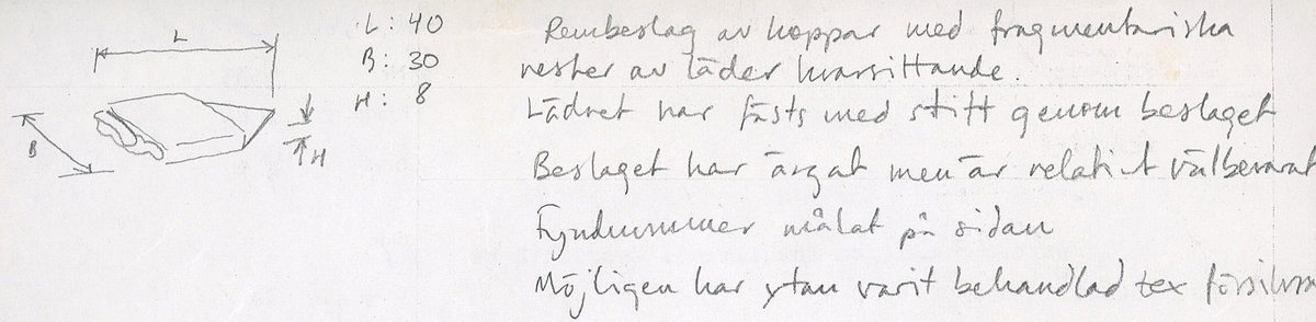 Remändebeslag av koppar med kvarsittande fragmentariska rester av läder. Lädret har fästs med stift genom beslaget. Beslaget är ärgat men relativt välbevarat.