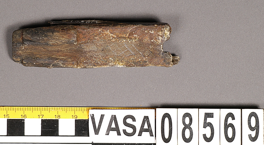 Bit av bösspipa. Bruten i bägge ändar. Diagonalt rutmönster på ena sidan.