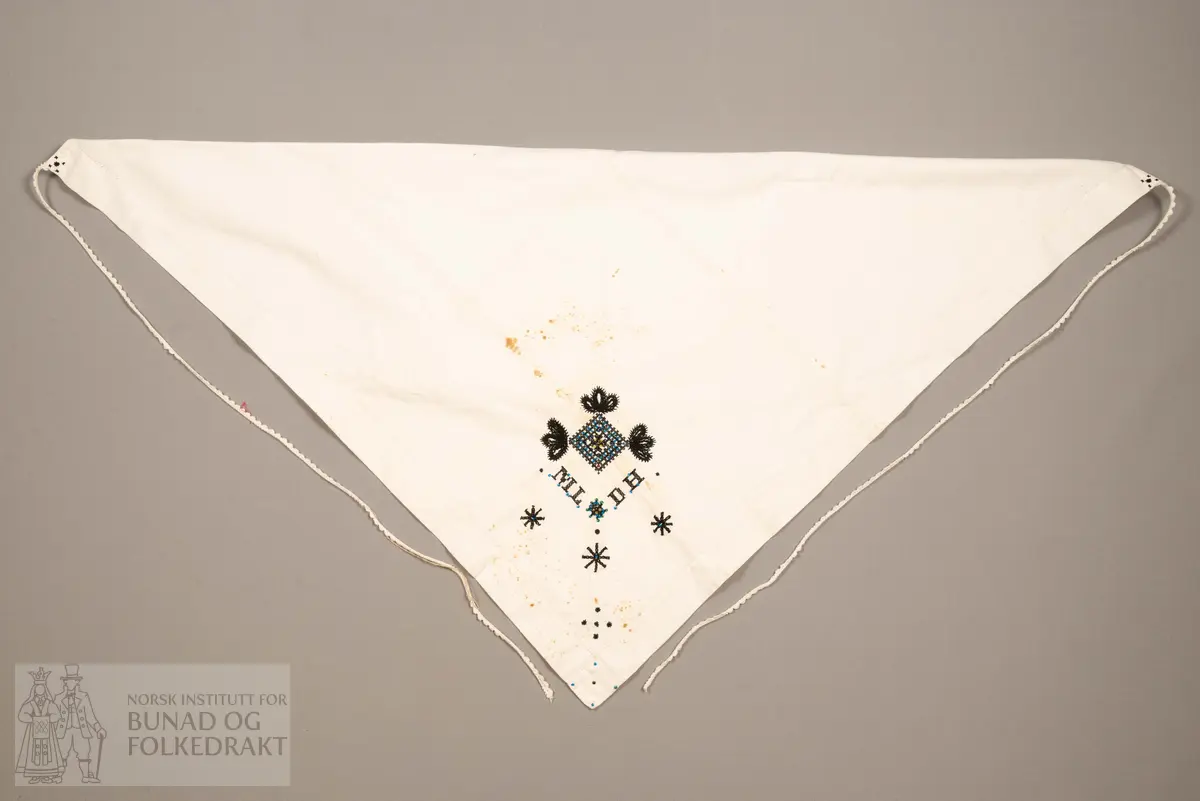 Skaut sydd av stødig, fast bomullslerret (24 tråder x 24 tråder per cm.). Bretta diagonalt. Broderi i eine snippen, av svart, tjukk silketråd og glasperler i mellomblå, mørk transparant blå, transparant grøn, transparant gul, og ei perle transparant raud.
Innbrodert med korssting initialane: "M.L.D.H."
Kjedesting, stilkesting og korssting.
Langs båe sider av den broderte snippen er bretta ein brei fald sydd ned med enkel holfald.
Også jare langs ei side og ein smalbretta fald sydd ned med små faldesting i den fjerde sida.
Knyteband av smalt, kvitt blondeband i bomull.

Om skautet i "Hovdatyet" av Eli Drønen: "Skautet var av lerret og sydd med svart tråd i korssting i nakken, ca. 67 x 67 cm. Skautebanda vart festa i to endar av skauten, dei er i ripsvevnad 58 cm x 1,3. Skautet vart lagt i trekant og sett på hua. Det vart kryssa bak, og skautspissane rakk til øyrene, og vidare vart skautebanda kryssa framme ca. 3 cm innpå skautet og ført vidare og knytt bak under skautet. Endene av banda vart putta innunder skautet. (...) Skautet var brukt utanpå rundhua, når dei gjekk til kyrkje, i gjestebod og i bryllaup."