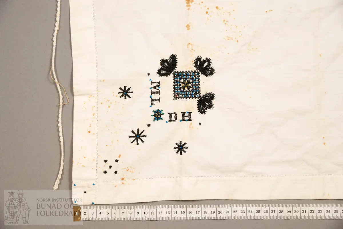 Skaut sydd av stødig, fast bomullslerret (24 tråder x 24 tråder per cm.). Bretta diagonalt. Broderi i eine snippen, av svart, tjukk silketråd og glasperler i mellomblå, mørk transparant blå, transparant grøn, transparant gul, og ei perle transparant raud.
Innbrodert med korssting initialane: "M.L.D.H."
Kjedesting, stilkesting og korssting.
Langs båe sider av den broderte snippen er bretta ein brei fald sydd ned med enkel holfald.
Også jare langs ei side og ein smalbretta fald sydd ned med små faldesting i den fjerde sida.
Knyteband av smalt, kvitt blondeband i bomull.

Om skautet i "Hovdatyet" av Eli Drønen: "Skautet var av lerret og sydd med svart tråd i korssting i nakken, ca. 67 x 67 cm. Skautebanda vart festa i to endar av skauten, dei er i ripsvevnad 58 cm x 1,3. Skautet vart lagt i trekant og sett på hua. Det vart kryssa bak, og skautspissane rakk til øyrene, og vidare vart skautebanda kryssa framme ca. 3 cm innpå skautet og ført vidare og knytt bak under skautet. Endene av banda vart putta innunder skautet. (...) Skautet var brukt utanpå rundhua, når dei gjekk til kyrkje, i gjestebod og i bryllaup."