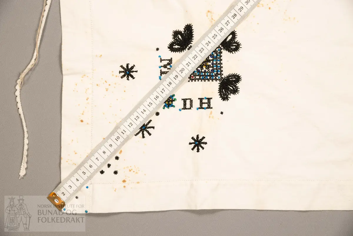 Skaut sydd av stødig, fast bomullslerret (24 tråder x 24 tråder per cm.). Bretta diagonalt. Broderi i eine snippen, av svart, tjukk silketråd og glasperler i mellomblå, mørk transparant blå, transparant grøn, transparant gul, og ei perle transparant raud.
Innbrodert med korssting initialane: "M.L.D.H."
Kjedesting, stilkesting og korssting.
Langs båe sider av den broderte snippen er bretta ein brei fald sydd ned med enkel holfald.
Også jare langs ei side og ein smalbretta fald sydd ned med små faldesting i den fjerde sida.
Knyteband av smalt, kvitt blondeband i bomull.

Om skautet i "Hovdatyet" av Eli Drønen: "Skautet var av lerret og sydd med svart tråd i korssting i nakken, ca. 67 x 67 cm. Skautebanda vart festa i to endar av skauten, dei er i ripsvevnad 58 cm x 1,3. Skautet vart lagt i trekant og sett på hua. Det vart kryssa bak, og skautspissane rakk til øyrene, og vidare vart skautebanda kryssa framme ca. 3 cm innpå skautet og ført vidare og knytt bak under skautet. Endene av banda vart putta innunder skautet. (...) Skautet var brukt utanpå rundhua, når dei gjekk til kyrkje, i gjestebod og i bryllaup."